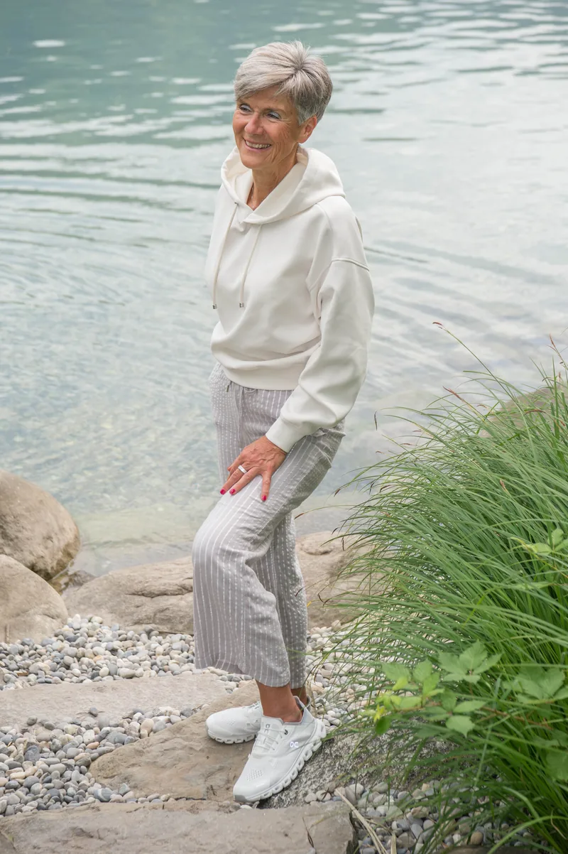 Désirée Ludwig in hellem Hoodie am Ufer, lächelnd.