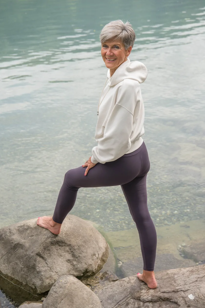 Désirée Ludwig steht auf einem Stein am See und blickt lächelnd über die Schulter.