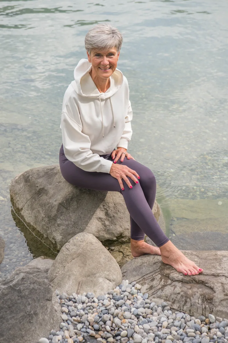 Désirée Ludwig sitzt auf einem Stein am Ufer und schaut ruhig zur Seite.